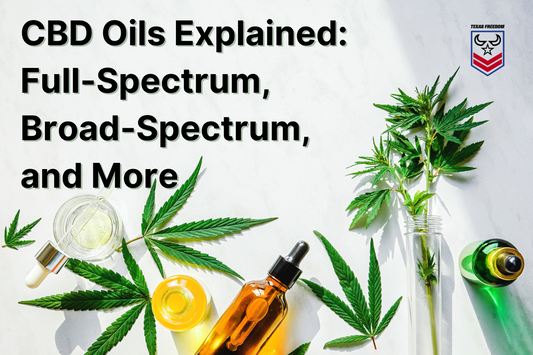 We have cannabis leaves and CBD oils laying on a white at Texas Freedom CBD Manufacturing, with the words "CBD Oils Explained: Full-Spectrum, Broad-Spectrum, and More" on top. 